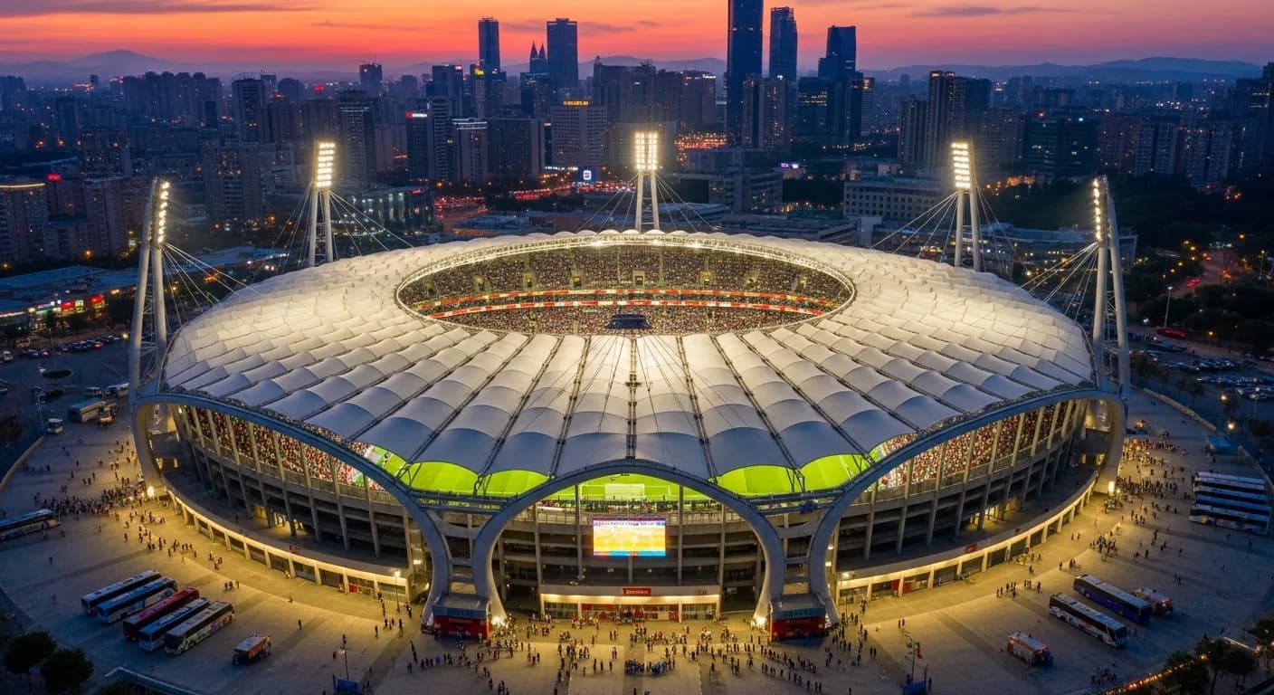 Aerial view of a large modern soccer stadium illuminated at sunset with fans gathering outside.